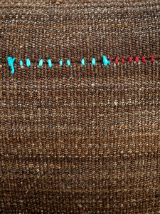 detail of sofa covered with vintage dark brown wool kilim fabric with coloured accents